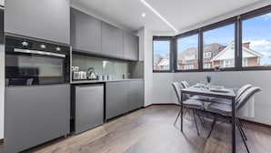 A modern kitchen with grey cabinets, a built-in oven, and a dining area with a table and chairs.