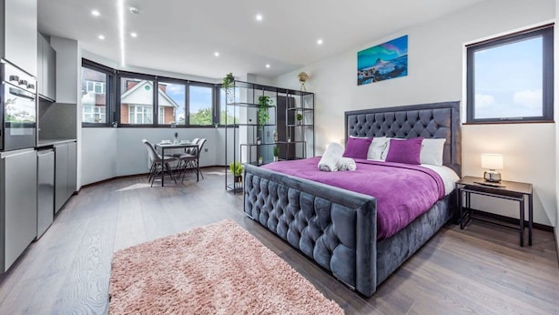 A modern bedroom with a large bed, a desk, and a view of the outside.