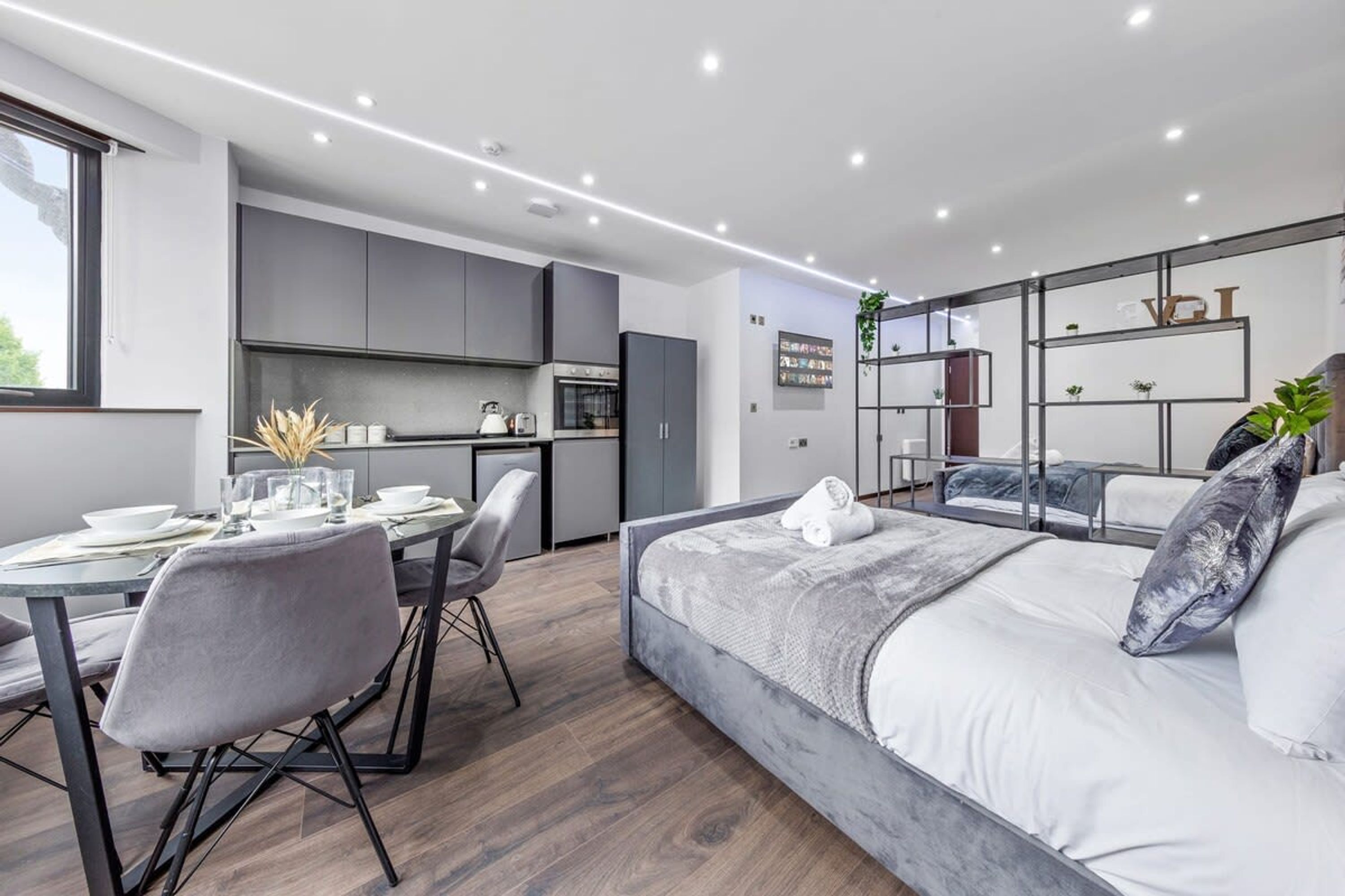 A modern, compact bedroom with a bed, bedside tables, and a small kitchenette.