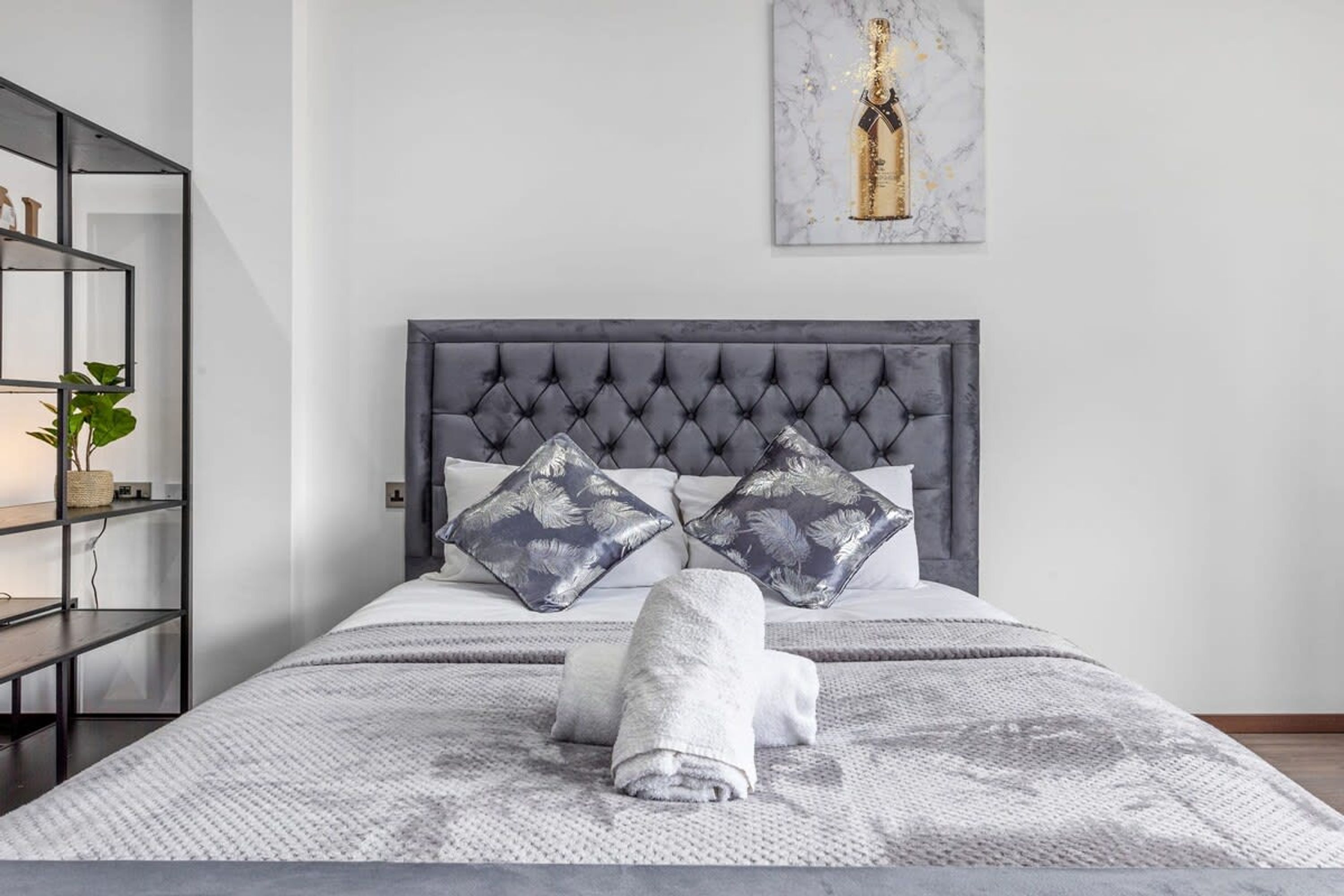A neatly made bed with a grey headboard, two decorative pillows, and a folded towel.