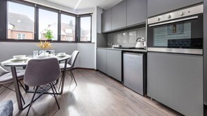 A modern kitchen with grey cabinets, a built-in oven, and a dishwasher. There is a dining table with chairs and a vase of dried flowers. - Serviced Studio Flat Near London Northern Line (London)