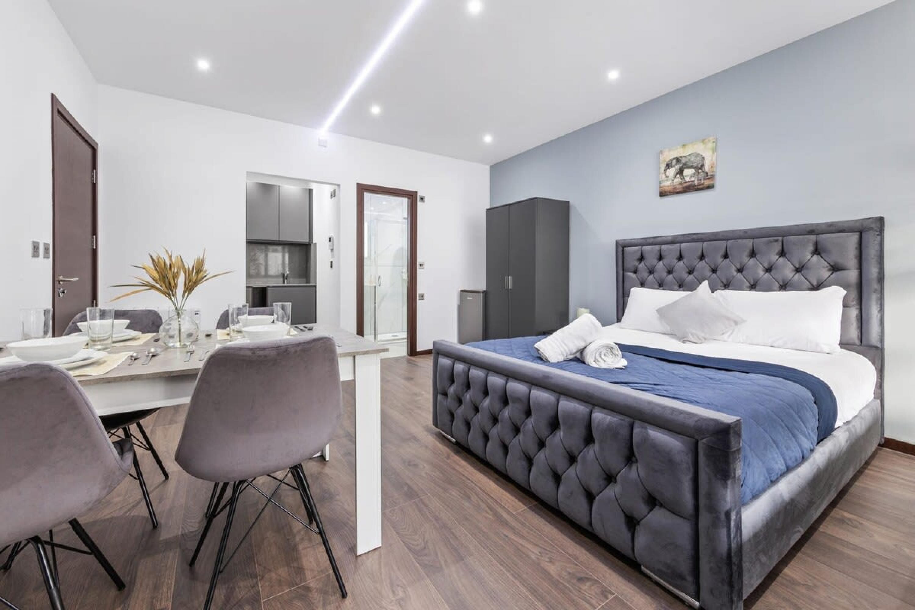 Een moderne slaapkamer met een groot bed, een eettafel met stoelen en een keukenhoek.