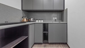 Cozinha compacta com armários cinza, chaleira de aço inoxidável, torradeira e cafeteira.