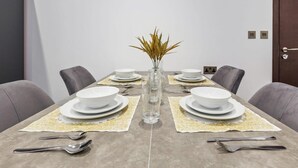 Uma mesa de jantar posta com pratos, tigelas, talheres e um vaso com plantas secas.