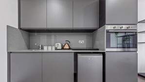 A compact kitchen with grey cabinetry, a built-in oven, and a small refrigerator.