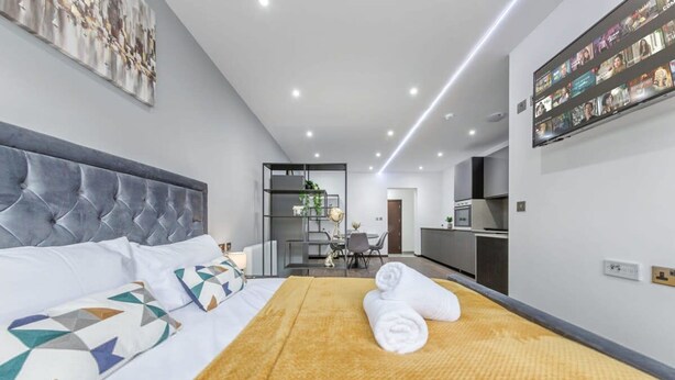 Een moderne hotelkamer met een groot bed, een zithoek en een keuken op de achtergrond.