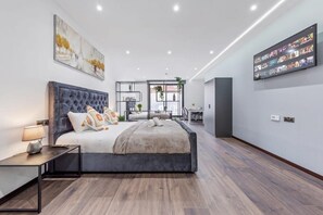 A modern bedroom with a large bed, a desk, and a TV wall. - Luxury Sleeps 4 Studio Flat (London)