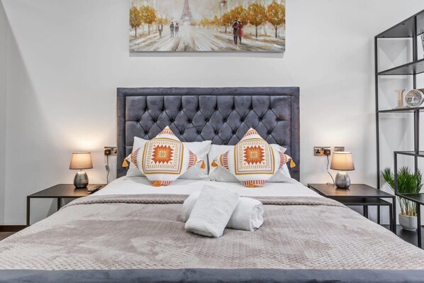 A neatly made bed with a tufted headboard, two bedside lamps, and decorative pillows. - Luxury Sleeps 4 Studio Flat (London)