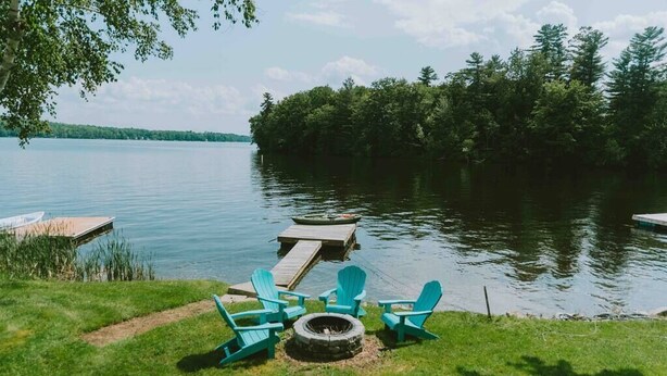 A lakeside deck with Adirondack chairs, a fire pit, and a dock extending into the water. - Little Landing Cottage-gorgeous View BBQ Wi-fi (Winthrop)