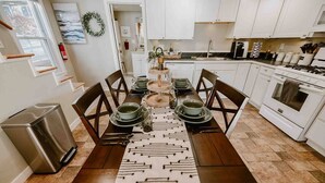 A modern kitchen with white cabinets, a stainless steel range hood, and a dining area with a wooden table and chairs. - Little Landing Cottage-gorgeous View BBQ Wi-fi (Winthrop)