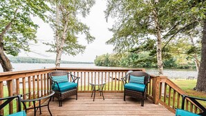 Une terrasse en bois avec deux fauteuils en osier et une petite table, donnant sur un lac.