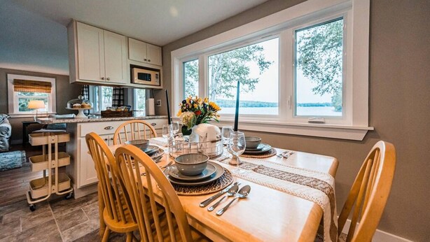Un coin repas avec une table dressée pour quatre personnes, une cuisine en arrière-plan et une vue sur les arbres par la fenêtre.