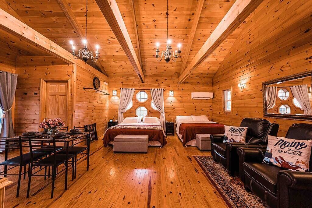 A log cabin interior with a dining area, two bedrooms, a living room with leather sofas, and a chandelier.