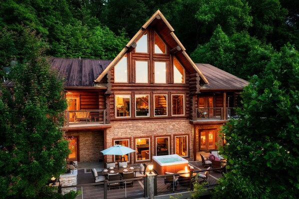 A log cabin with a large deck, outdoor seating, and a hot tub.