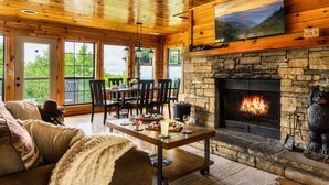Interior acogedor de una cabaña con chimenea de piedra, techo de madera y ventanas amplias con vistas al exterior.