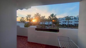 Un balcon avec vue sur les palmiers et un coucher de soleil.