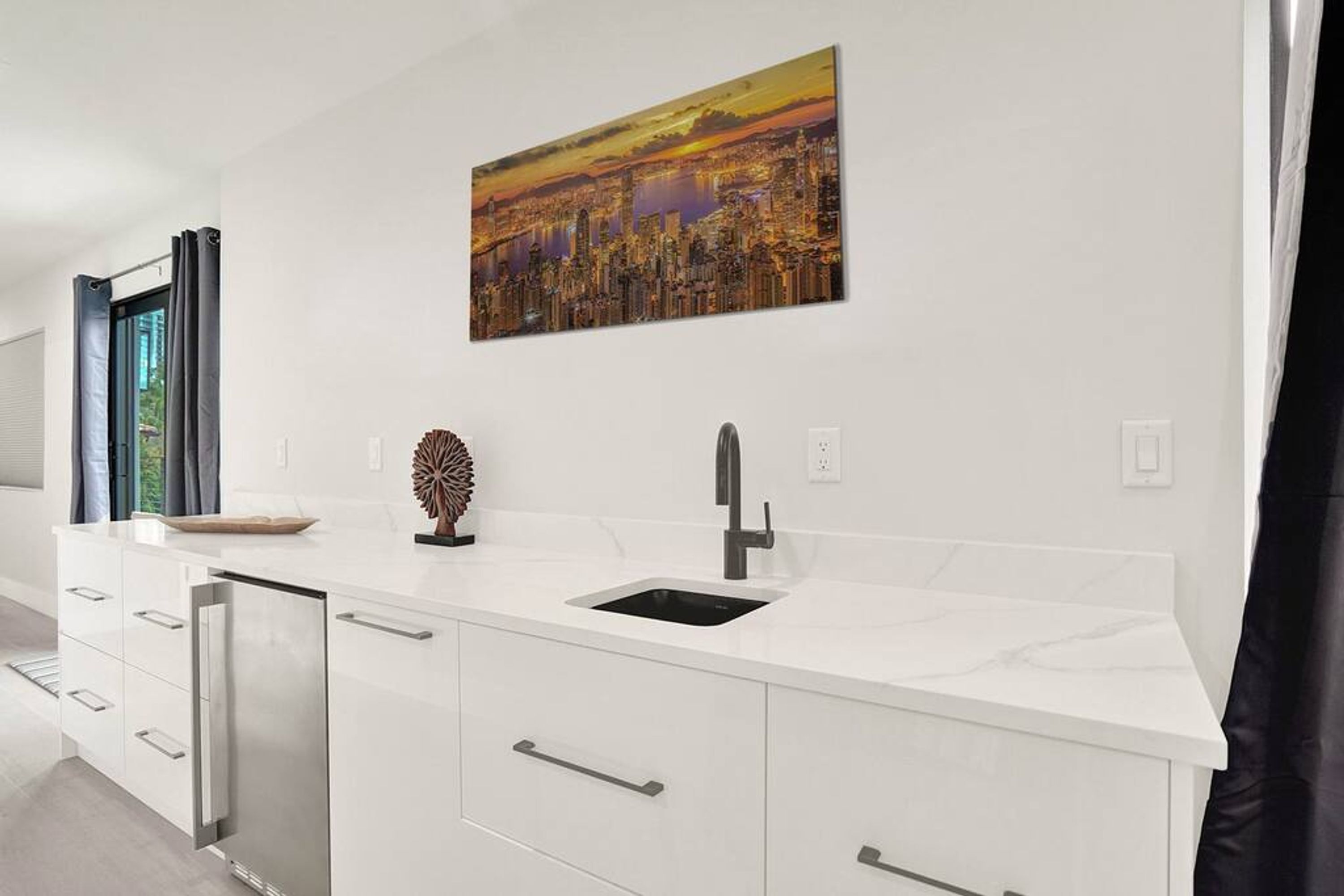 A modern kitchen with a white countertop, stainless steel appliances, and a cityscape painting above the sink.