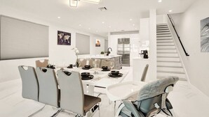 Un comedor moderno con una mesa blanca dispuesta para cuatro personas, rodeada de sillas grises. Se ve un cochecito de bebé al frente.