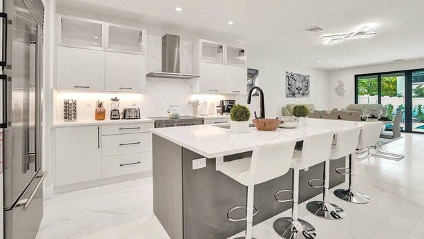 Una cocina moderna con una isla central, taburetes de bar y un comedor con vistas a la piscina.