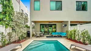 Un edificio moderno con piscina, mobiliario exterior y un patio cubierto.