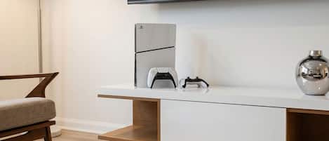 A modern living room with a flat-screen TV mounted on the wall, a white console table with a game controller, a vase, and a chair.