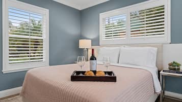 A bedroom with a bed, a tray with wine and pastries, a lamp, and a book on a nightstand.