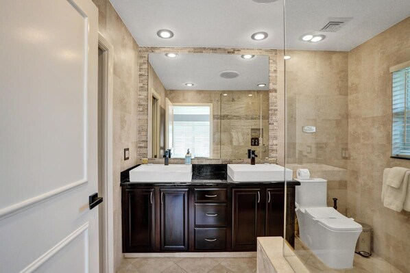 A modern bathroom with a dual sink vanity, dark cabinetry, a glass shower enclosure, and a toilet.