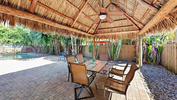 Un patio al aire libre con techo de paja, piscina y zona de comedor con sillas y mesa.