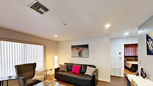 Una sala de estar moderna con una mesa de centro de vidrio, un sofá de cuero y una zona de comedor con una mesa y sillas blancas.