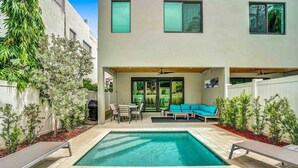 A modern outdoor pool area with a rectangular pool, a covered seating area with a sofa and chairs, and a small table. - Luxury Paradise Walk to Las Olas -5 Mins to Beach (Fort Lauderdale)