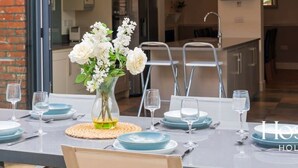 A dining area with a table set for four, a vase of flowers, and a kitchen in the background. - Marlow s Hidden Gem (Marlow)
