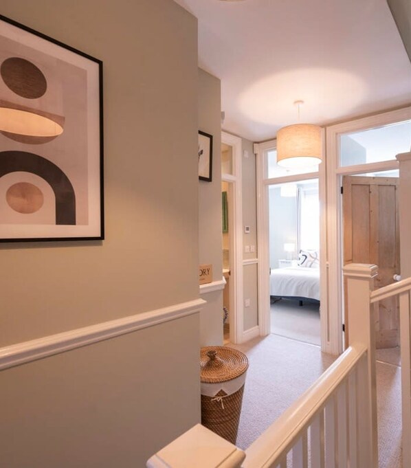 A hallway leading to a bedroom with a bed, a hanging light fixture, and a staircase.
