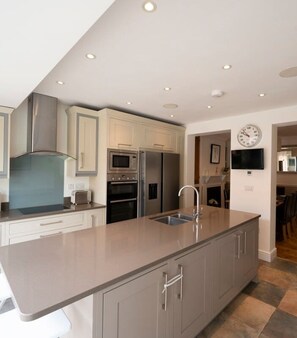 A modern kitchen with stainless steel appliances, a large island, and a dining area visible through an open doorway.
