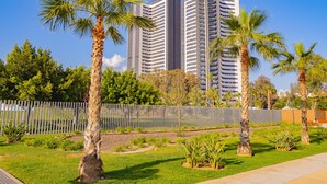Un edificio moderno de gran altura con una fachada curva distintiva, rodeado de palmeras cuidadas y un área verde con una cerca de metal.