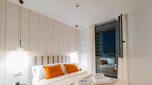 Una habitación de hotel moderna con una cama grande, dos almohadas, una mesita de noche y una ventana con vistas a la ciudad.