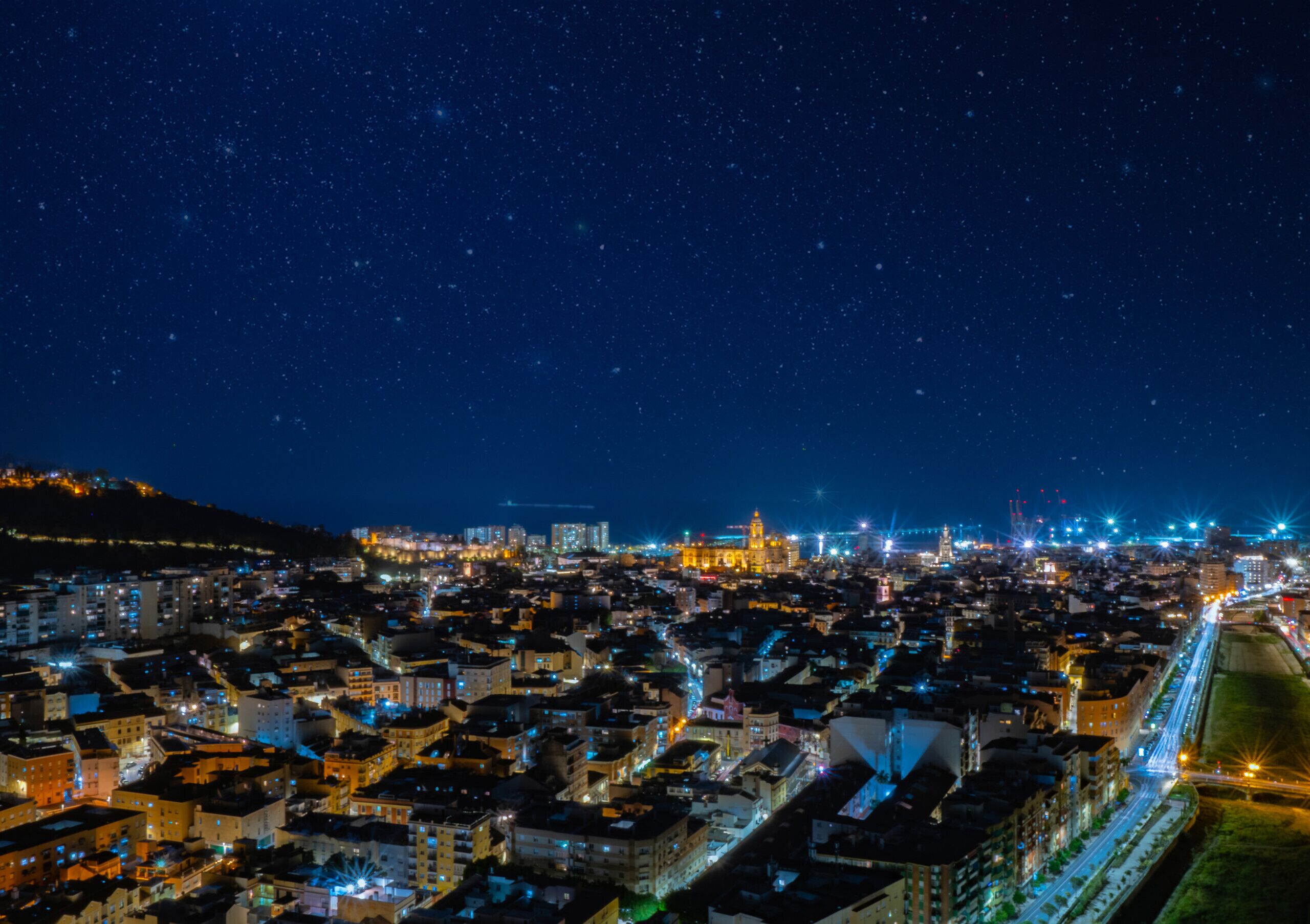 Une vue nocturne d’une ville, avec des bâtiments illuminés et un ciel étoilé.