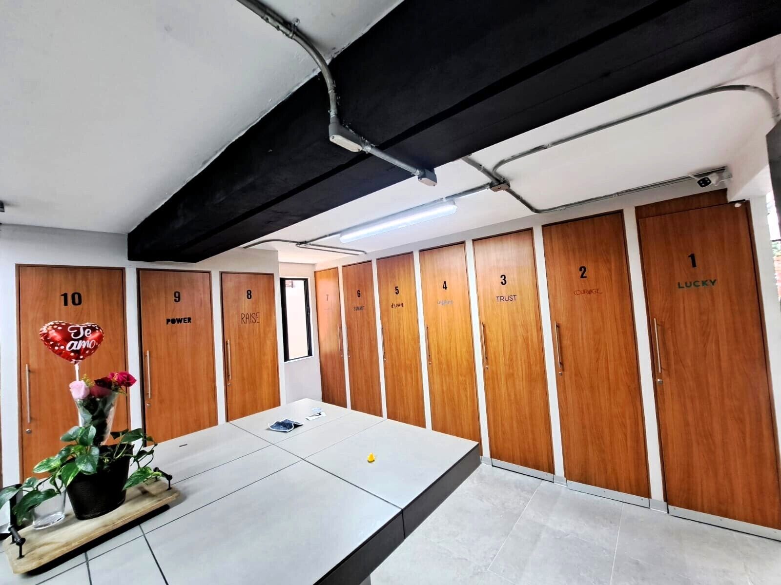 A locker room with numbered lockers, a table with a plant, and a heart-shaped balloon.