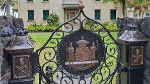 A wrought iron gate with a central emblem featuring a coat of arms and a statue of a figure. - Condo in the center of Kona, 2-unit AC, Washer/Dryer, Full Kitchen, Free Parking (Kailua-Kona)