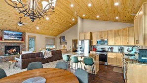 Amplia sala de estar con chimenea, mesa de comedor y cocina con gabinetes de madera y electrodomésticos modernos.
