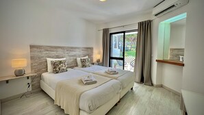 Habitación de hotel con dos camas, un ventanal grande, una lámpara de techo, un equipo de aire acondicionado y una mesita de noche con lámpara.