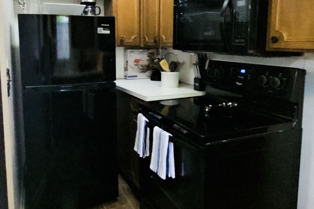 Una cocina con electrodomésticos negros, armarios de madera y encimera blanca.