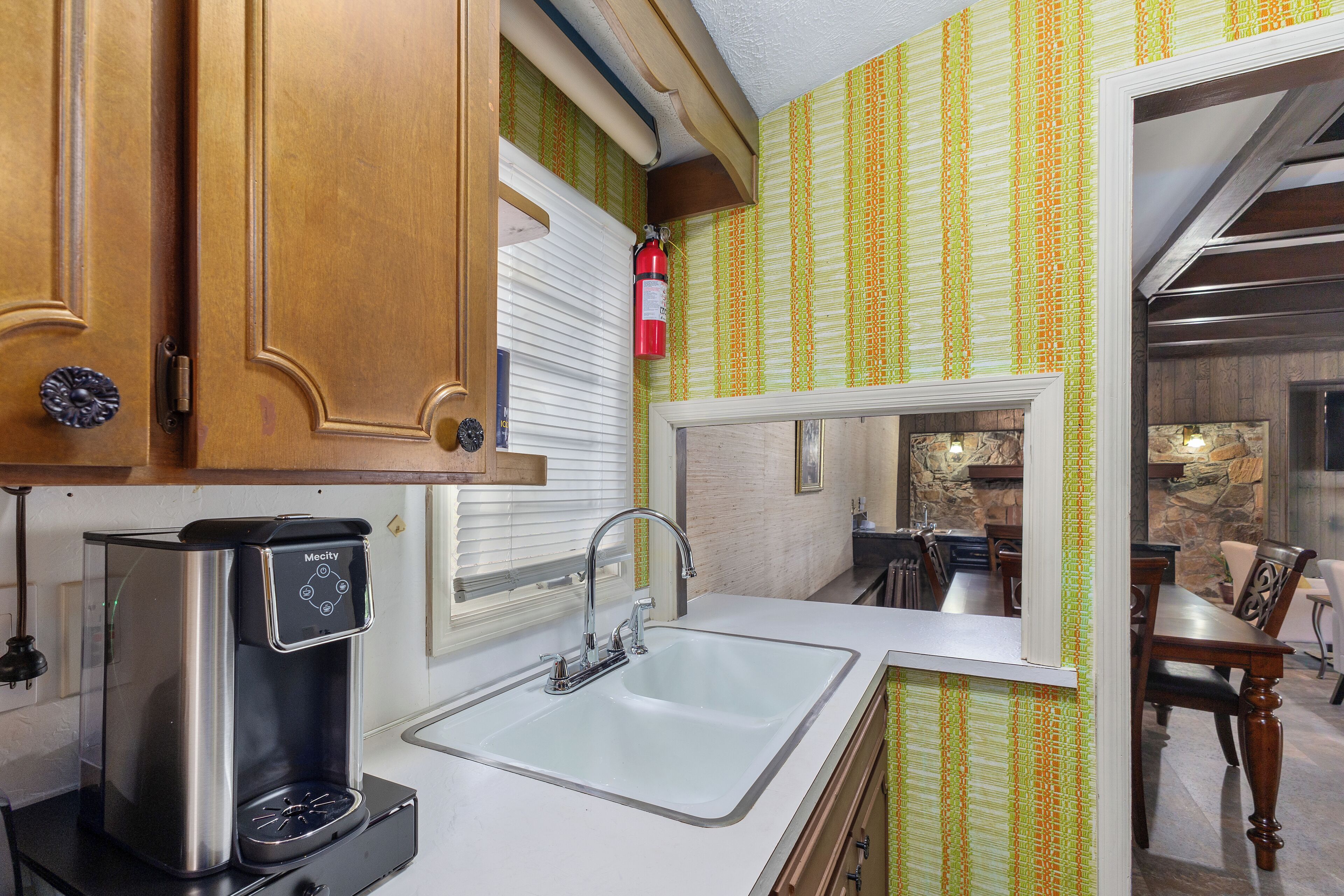A compact kitchen with a coffee maker, a sink, and a dining area visible through an open door.