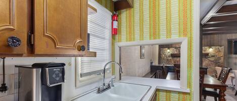 A compact kitchen with a coffee maker, a sink, and a dining area visible through an open door.