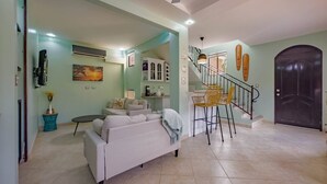 Un amplio espacio de estar con sofá, una mesa de comedor con sillas, una escalera y una puerta oscura.