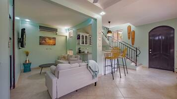 A spacious living area with a sofa, a dining table with chairs, a staircase, and a dark door.