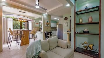 A modern living room with a sofa, a dining area with chairs, a kitchen with cabinets, and a ceiling fan.