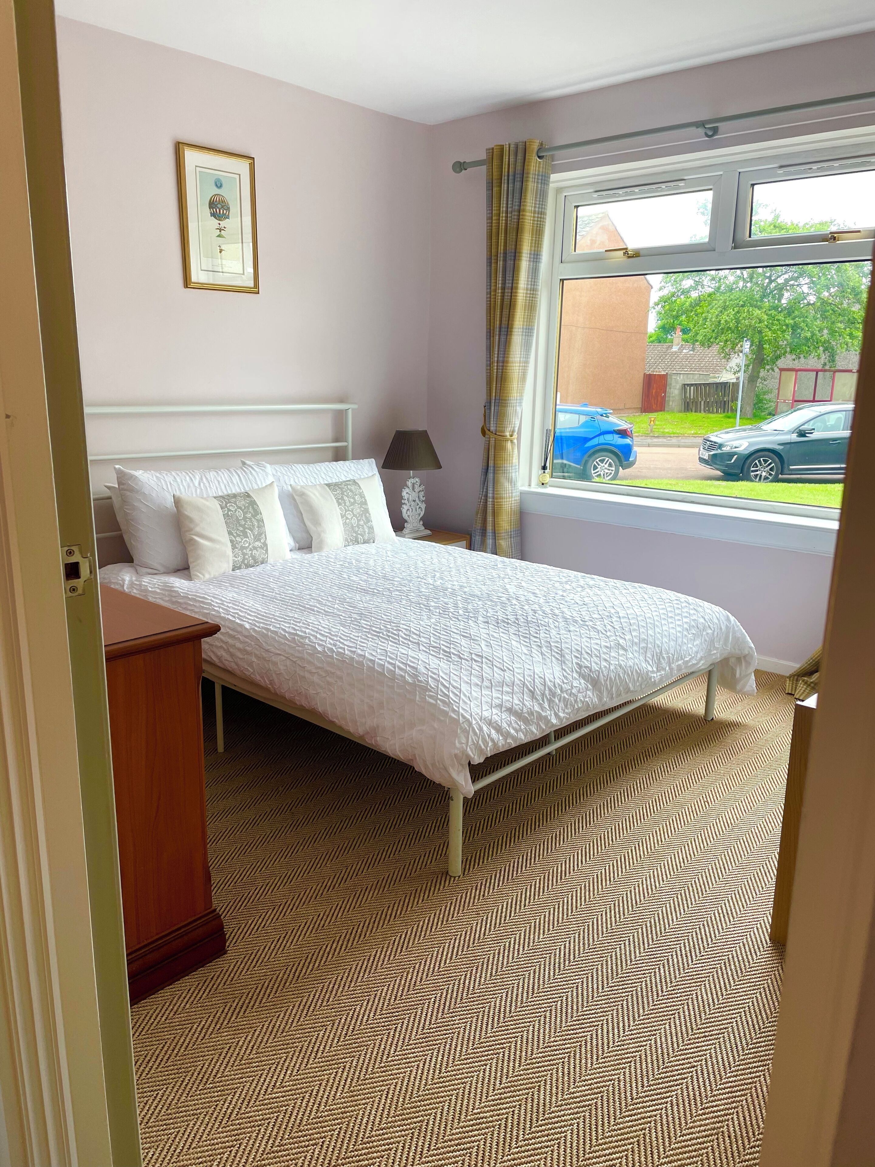 Quarto com cama, mesa de cabeceira, abajur, janela com cortinas e porta.