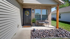 A house with a front porch, a black door with a wreath, a potted plant, and a bench. - Laura’s Simply Charming Home on Harrison (Quincy)