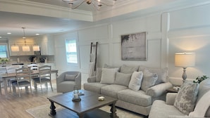 A spacious living room with a grey sofa, a coffee table, and a dining area with a chandelier. - Laura’s Simply Charming Home on Harrison (Quincy)