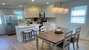 A modern kitchen with white cabinetry, stainless steel appliances, and a wooden dining table with four chairs. - Laura’s Simply Charming Home on Harrison (Quincy)